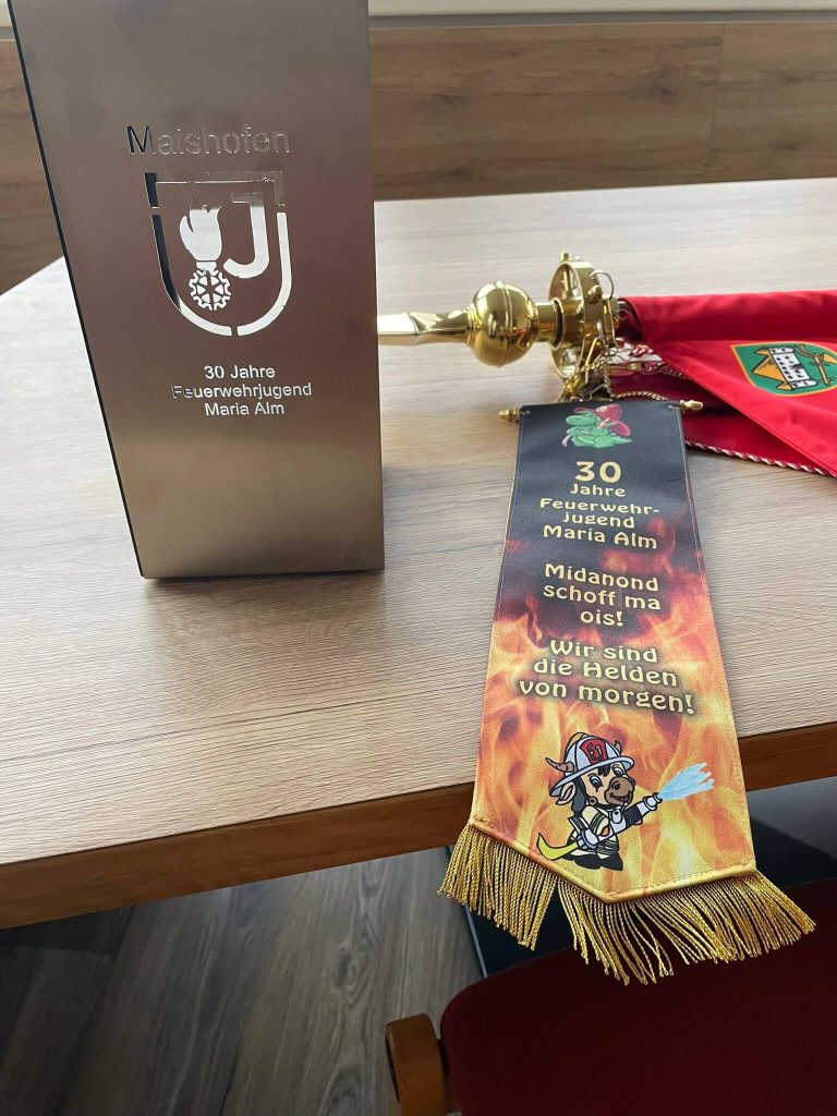Pokale und Banner zum 30-jährigen Jubiläum der Feuerwehrjugend Maria Alm auf Holztisch