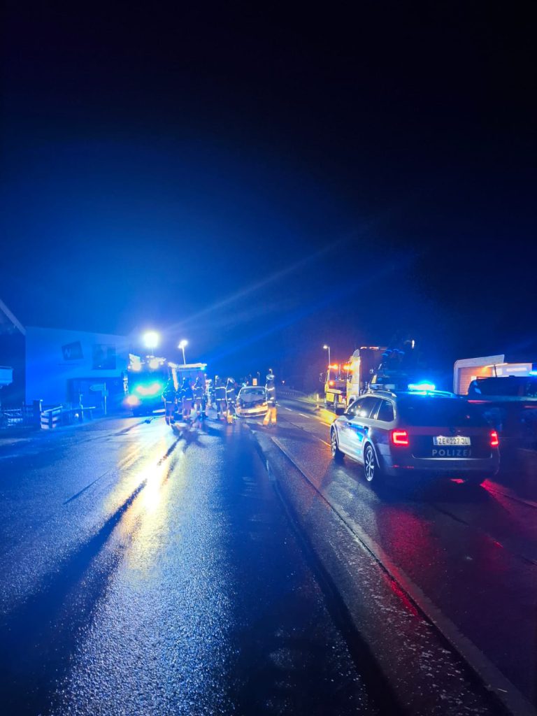 Feuerwehrleute in Schutzkleidung bei nächtlichem Einsatz vor beleuchtetem Löschfahrzeug