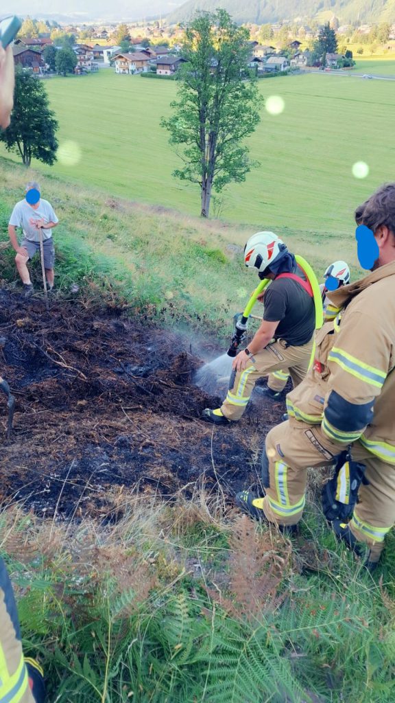 Feuerwehr löscht Flurbrand am Hang mit Schlauch und Schutzkleidung