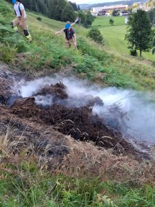 Feuerwehr löscht Glutnester auf bewachsenem Hang mit Schaufeln