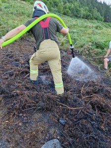Feuerwehrmann löscht Glutnester im Wald mit Wasserschlauch nach Flächenbrand