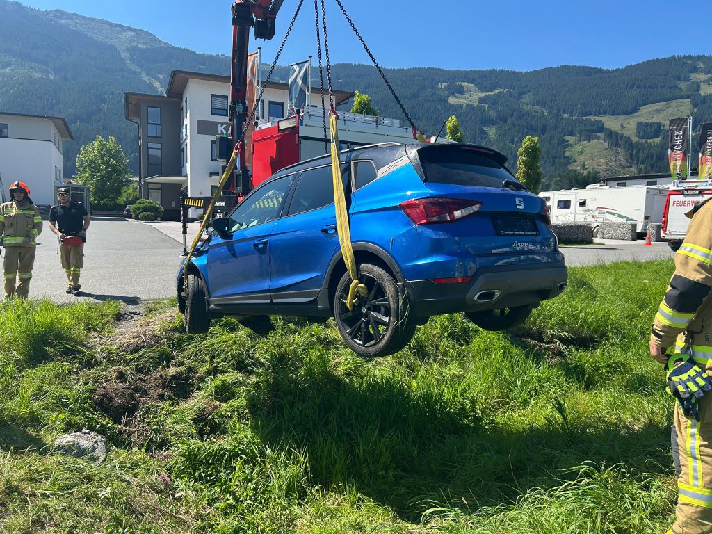 Feuerwehr hebt blaues Auto mit Kran nach Verkehrsunfall auf Wiese