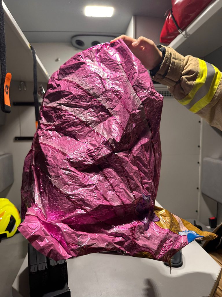 Feuerwehrkraft hält zerknitterten pinken Folienballon in Fahrzeugkabine