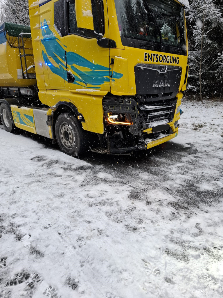 Gelber LKW mit beschädigter Frontpartie steht im Schneefall auf verschneiter Straße