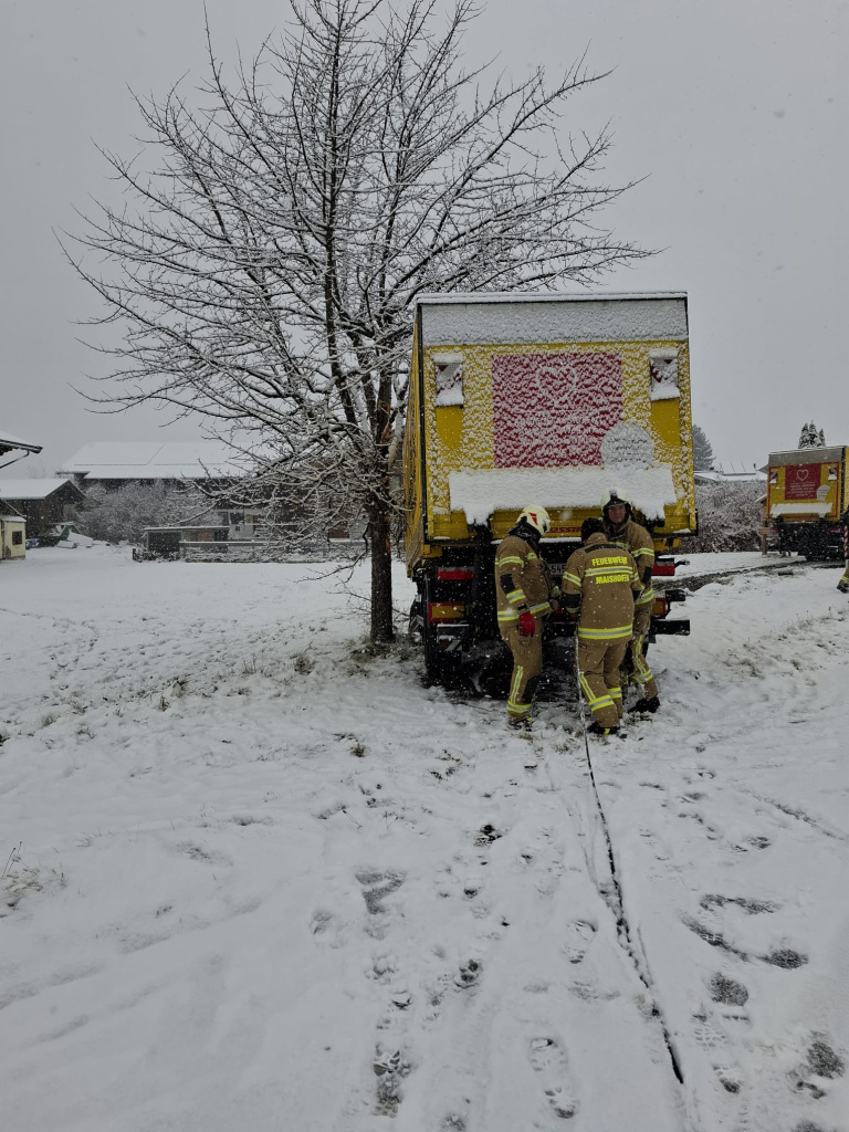 Feuerwehrkräfte sichern einen im Schnee von der Straße gerutschten LKW am Heckbereich