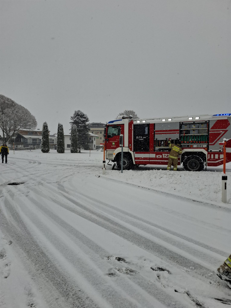 Feuerwehrfahrzeug steht bei Schneefall am Straßenrand, Einsatzkraft daneben