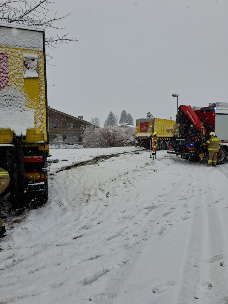 Feuerwehrkräfte bergen im Schnee einen von der Straße gerutschten LKW mit Kran