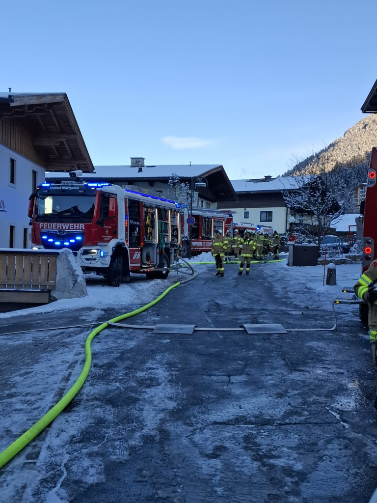 Feuerwehrfahrzeuge und Einsatzkräfte mit Schläuchen auf verschneiter Straße vor Hotelgebäuden