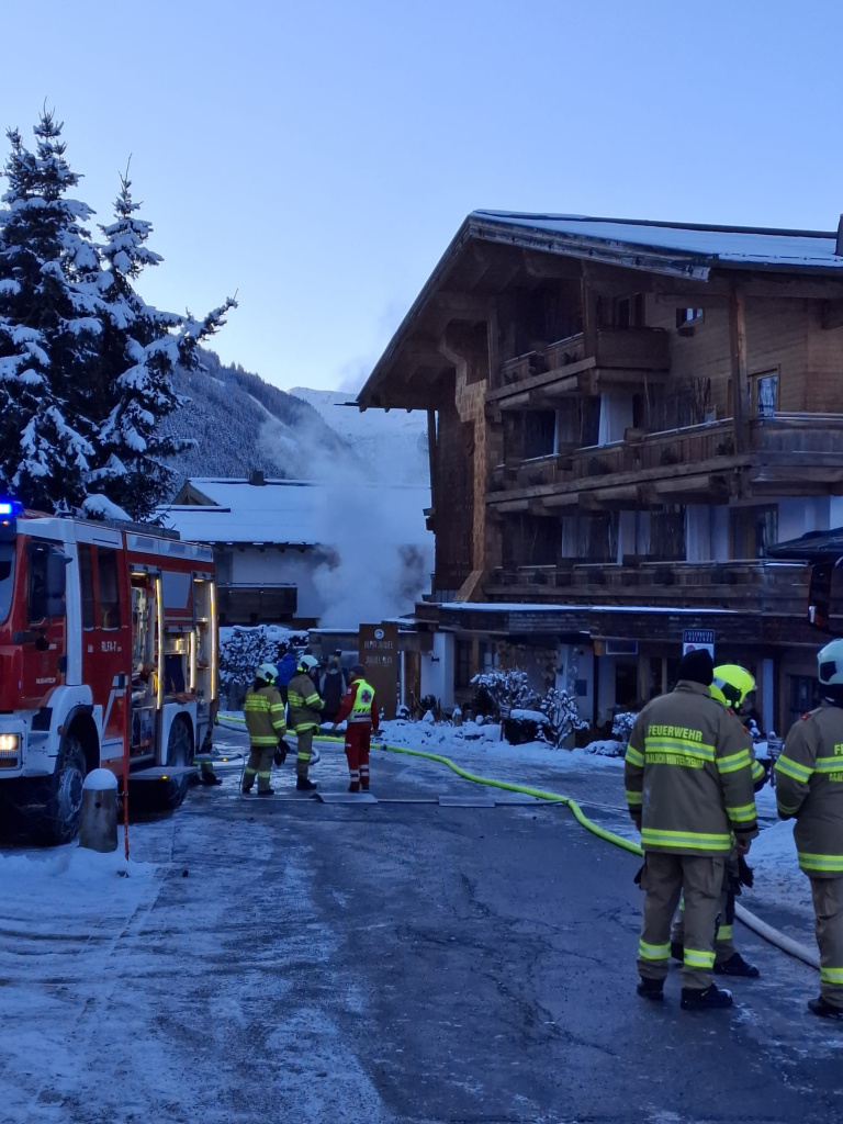 Feuerwehrkräfte arbeiten vor einem rauchenden Hotelgebäude in verschneiter Umgebung